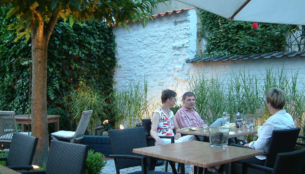 Gasten aan een tafeltje in de tuin van een restaurant bij avond